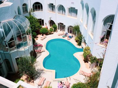 Blick auf einen herzförmigen Pool in einem weißen Hotelinnenhof mit Liegestühlen und Pflanzen.