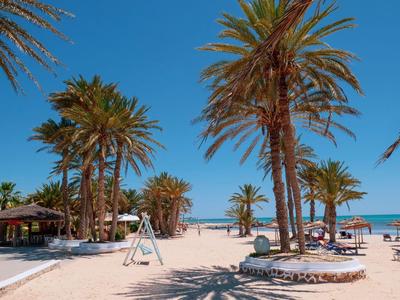 Strand mit Palmen, Sonnenliegen und klarem blauem Himmel an einem sonnigen Tag.
