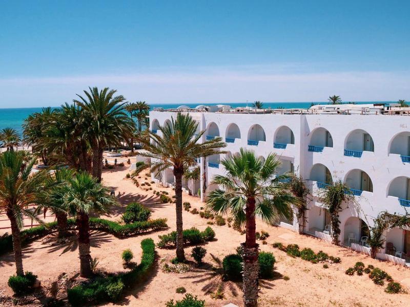 White hotel buildings with arches and palm trees against blue sky and sea.