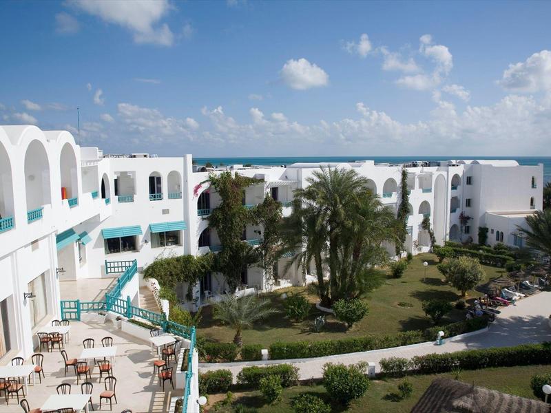 View of a white Mediterranean-style hotel with garden under blue sky.