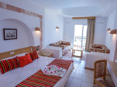 Hell eingerichtetes Zimmer mit zwei Einzelbetten, Sofa, Fliesenboden und Balkon mit Meerblick.