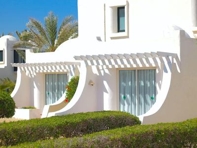 Weißes modernes Haus mit Rundbögen, großen Fenstern und grüner Gartenanlage bei klarem Himmel.