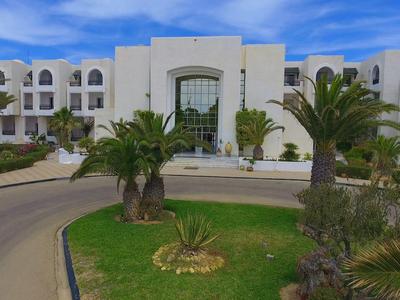 Weißes Hotelgebäude mit Palmen und grünem Rasengrundstück bei klarem Himmel