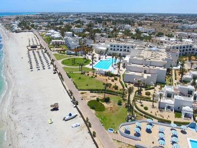 Langer Sandstrand mit klarem blauem Wasser, angrenzend an Hotelanlagen und Grünflächen.