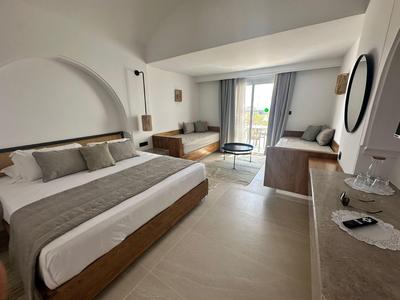 Modernes Schlafzimmer mit großem Bett, Holzmöbeln, Sofa, rundem Spiegel und Balkonzugang.