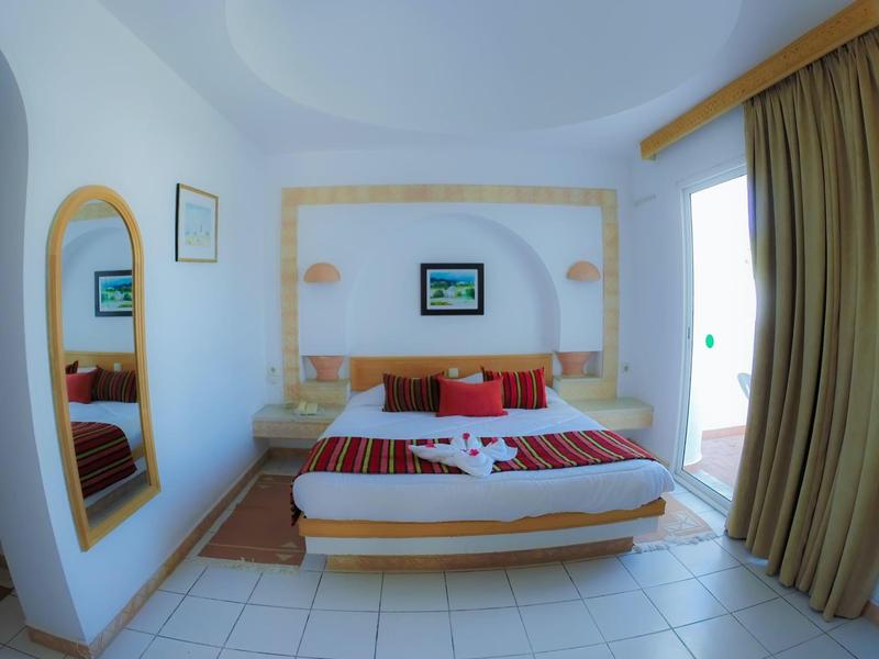 Helles Hotelzimmer mit Doppelbett, Wandspiegel und Zugang zu einem Balkon oder Terrasse.