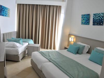 Helle Hotelzimmer mit zwei Betten, türkisfarbenen Akzenten und großem Fenster mit Vorhängen.