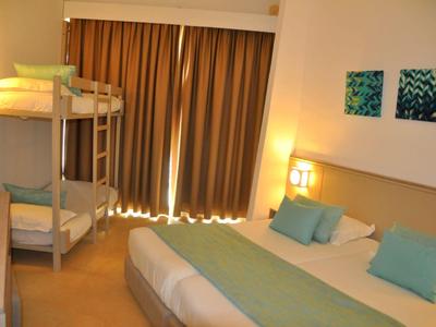 Hell eingerichtetes Hotelzimmer mit Doppelbett, Stockbett und Vorhängen.