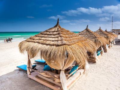 Reihe von Strohdach-Liegen am weißen Sandstrand mit türkisfarbenem Meer im Hintergrund.