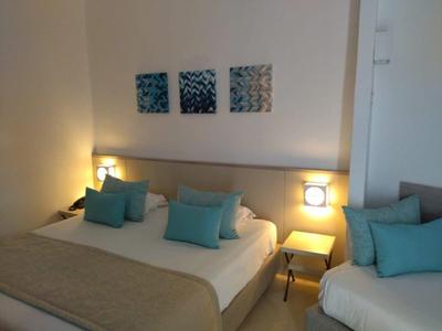 Modernes Hotelzimmer mit zwei Betten, blauen Kissen und drei abstrakten Bildern an der Wand.