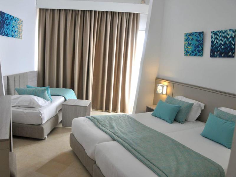 Hotelzimmer mit Doppel- und Einzelbett, blauen Akzenten und Vorhängen am Fenster