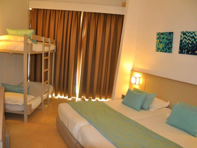 Hell eingerichtetes Hotelzimmer mit Doppelbett, Stockbett und Vorhängen.