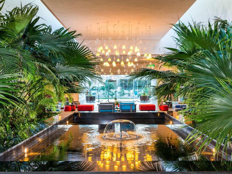 Moderner Hotel-Eingangsbereich mit Wasserbecken und Palmen links und rechts.