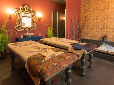 Gemütlicher Raum mit zwei Massageliegen, dekorativem Spiegel, Pflanzen und warmen Farben an Wänden.