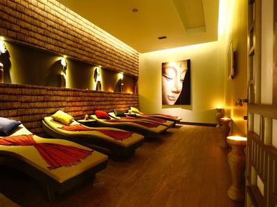 Ein warm beleuchteter Ruheraum mit Liegen, Backsteinwand und modernem Wandbild.