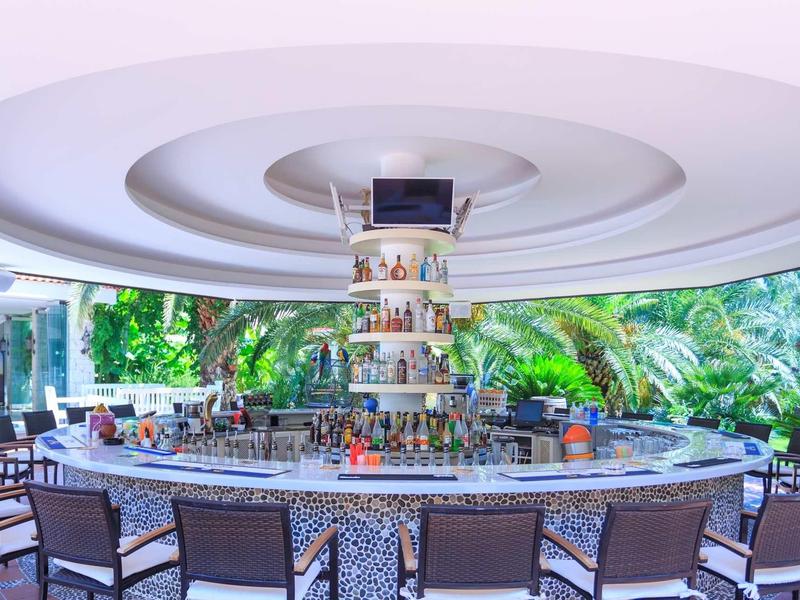 Runder Außenbarbereich mit hoher Decke, Holzstühlen und grüner Umgebung im Hintergrund.