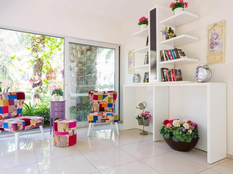 Heller, moderner Raum mit bunten Sesseln, Glasfenster, weißen Regalen und blühenden Pflanzen.