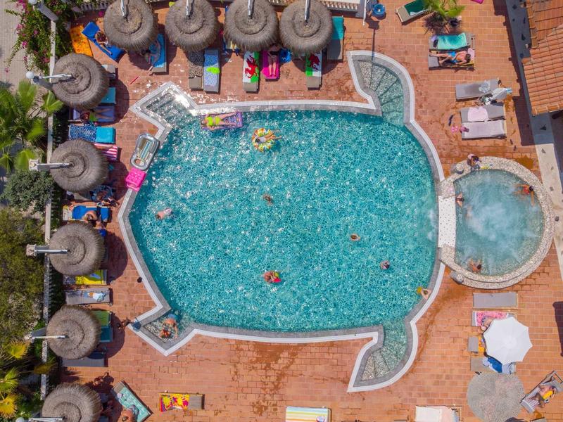 Luftaufnahme eines rechteckigen Pools mit runden Ecken, Sonnenliegen, Schirmen und Personen im Wasser.