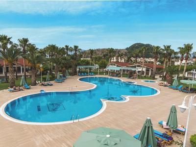 Großer, geschwungener Pool in Hotelanlage mit Liegestühlen, Palmen und blauem Himmel.