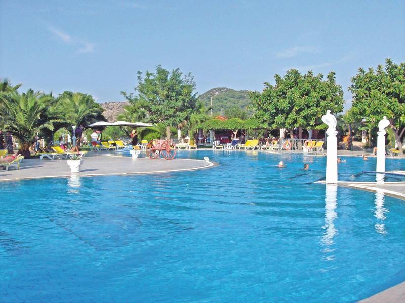 Velký hotelový bazén obklopený slunečnímiky a palmami pod jasnou oblohou.