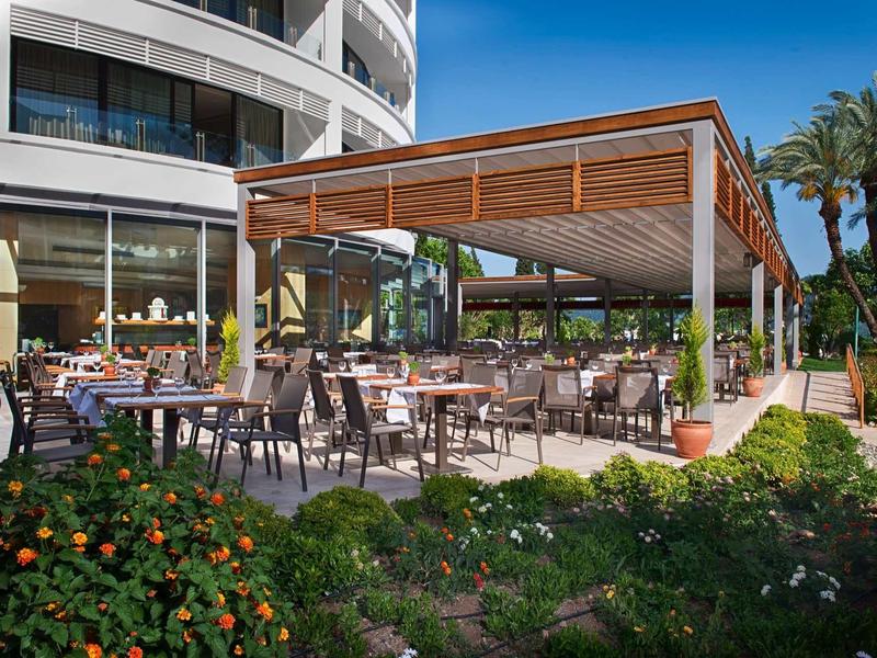 Moderna área exterior de hotel con asientos cubiertos y jardín bajo el sol.