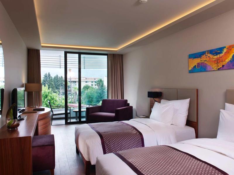 Habitación de hotel moderna con dos camas individuales, TV, balcón y arte colorido en la pared.