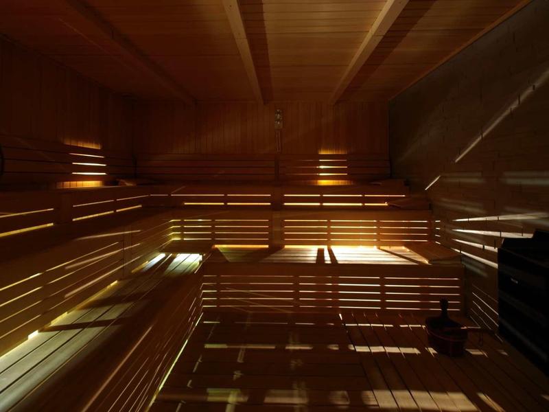 Interior de una sauna con bancos de madera y juego de luces cálidas en las paredes.