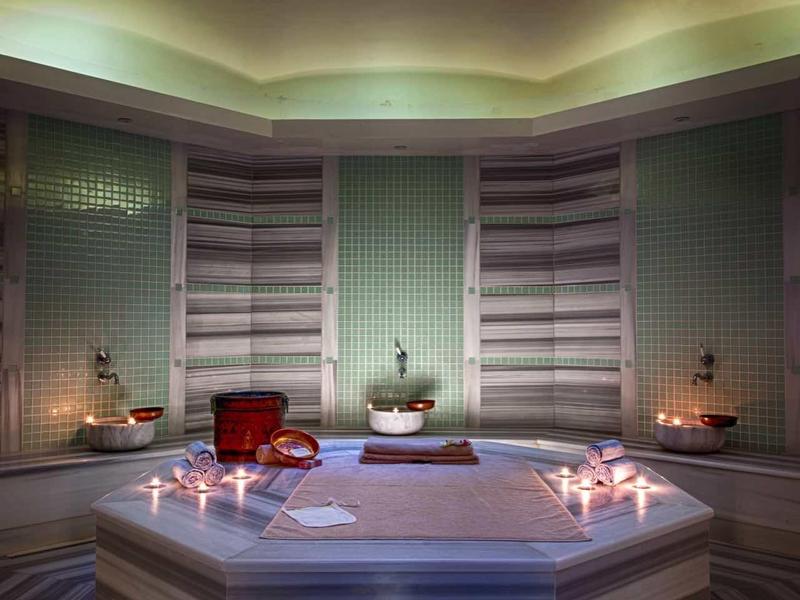 Sala de spa con piscina central hexagonal, iluminación suave y techo iluminado con luces azules.