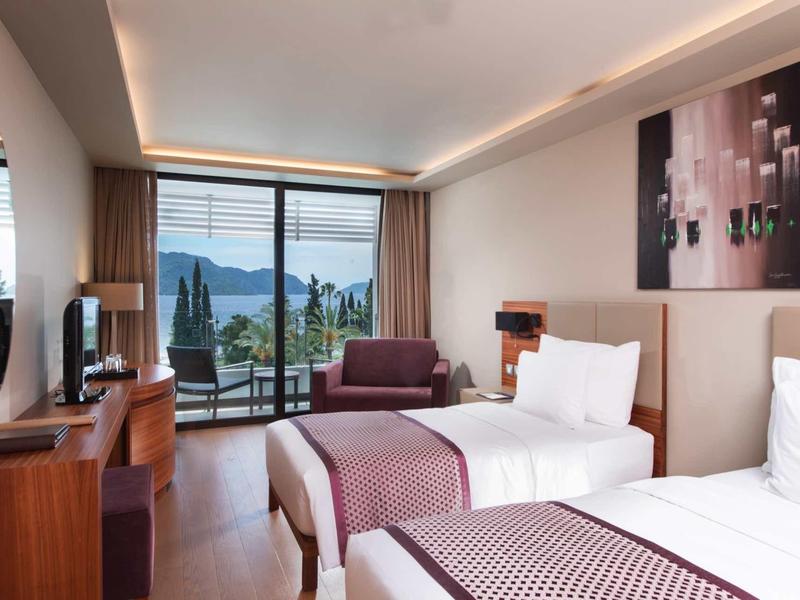 Habitación de hotel moderna con dos camas, balcón y vista a montañas y lago.