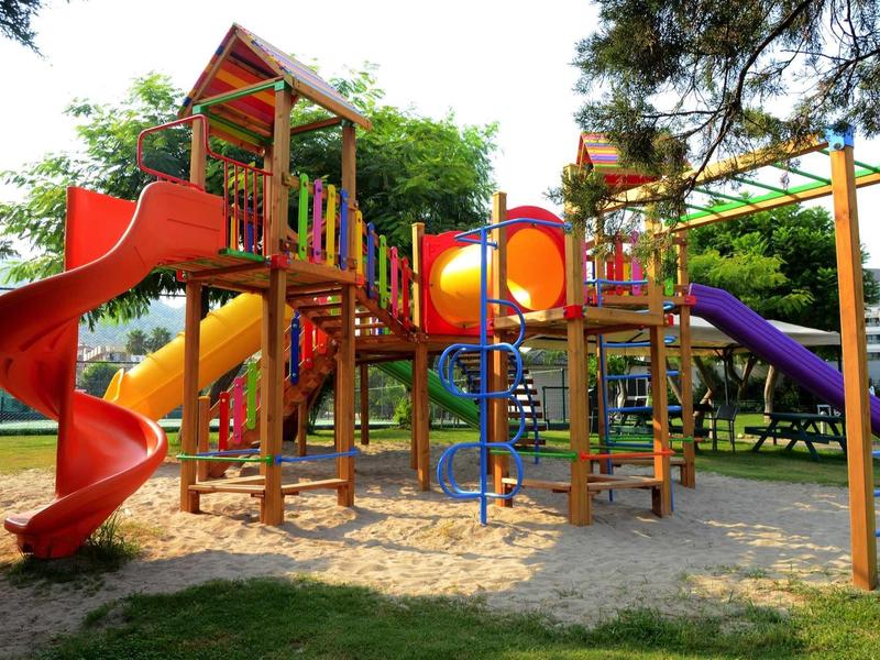 Parque infantil colorido con varios toboganes y estructuras para escalar bajo árboles.