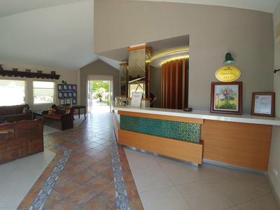 Bright hotel lobby with reception desk, seating area, and entrance to a garden.