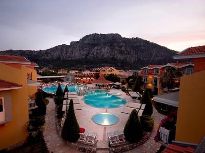 Evening view of a resort pool surrounded by buildings and mountains in the background.