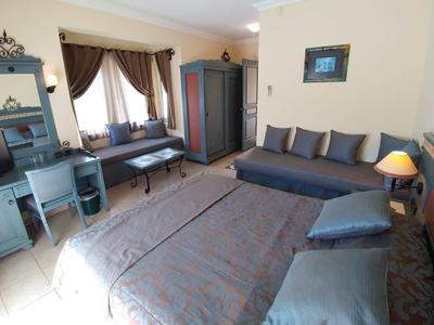 Cozy hotel room with bed, sofa, wardrobe, and desk in neutral tones.