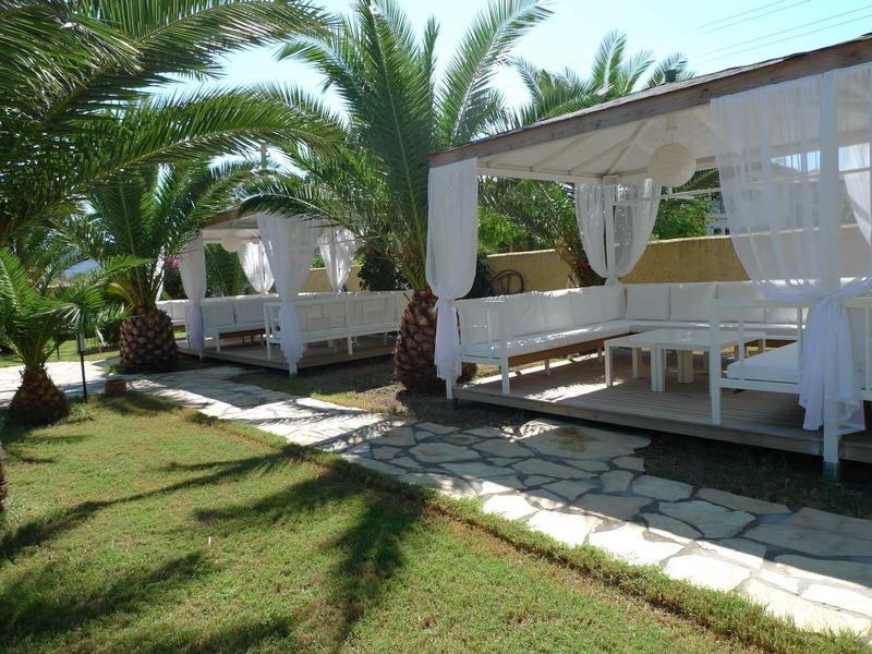 White pavilion with curtains and seating next to palm trees by the hotel pool garden.