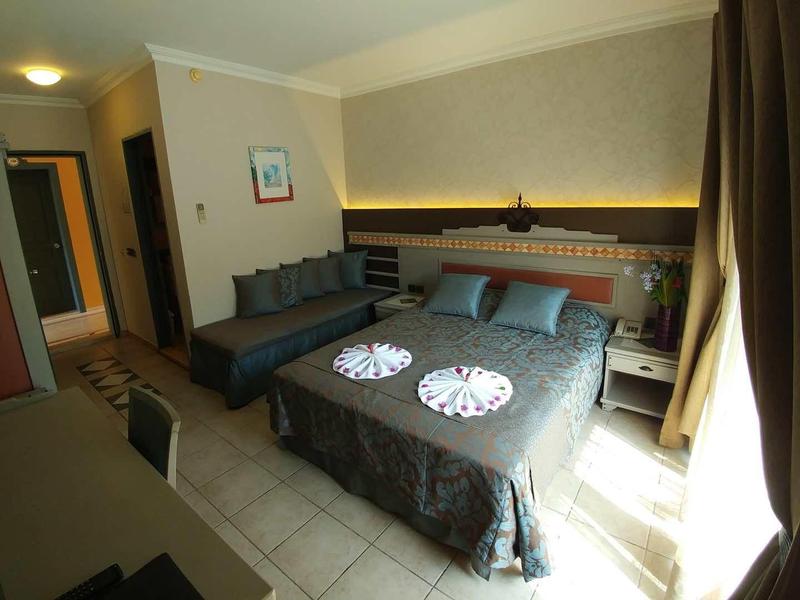 Bright hotel room with double bed, sofa, desk, and window with curtains