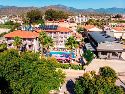 Blick auf ein Hotel mit Pool, Palmen und Bergen im Hintergrund bei klarem Himmel.