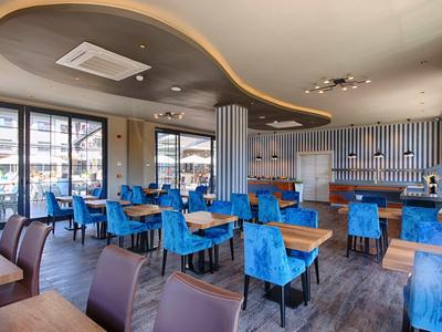 Salle à manger d'hôtel moderne avec des chaises bleues et de grandes fenêtres laissant entrer la lumière du jour.