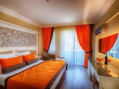 Chambre d'hôtel moderne avec lit double, literie et rideaux orange, sol en bois clair et balcon.