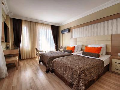 Helles Hotelzimmer mit zwei Einzelbetten, orangefarbenen Kissen und einem Schreibtisch am Fenster.