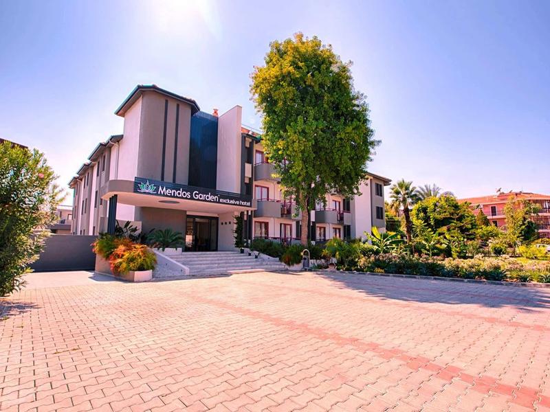 Bâtiment d'hôtel moderne avec parking et arbres sous un ciel ensoleillé.