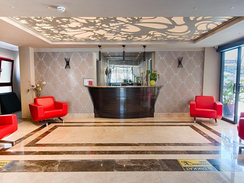 Hall d'hôtel lumineux avec comptoir de réception noir, fauteuils rouges et grande fenêtre donnant sur l'extérieur.