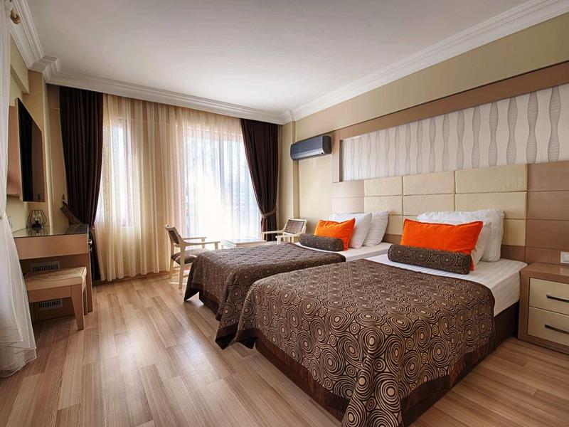 Chambre d'hôtel moderne avec deux lits, sol en bois et grandes fenêtres avec rideaux.