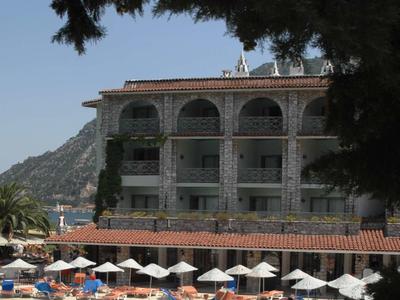 Ein Hotel mit Balkonzimmern neben einem großen blauen Pool, von Bäumen teilweise umrahmt.