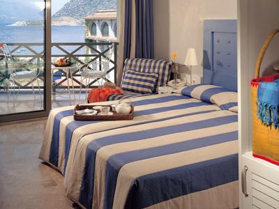 Helles Schlafzimmer mit blau gestreiftem Bett, Balkon und Meerblick im Hintergrund.