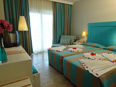 Helles Schlafzimmer mit zwei Einzelbetten, türkisfarbenem Kopfteil und Balkon mit Vorhängen.