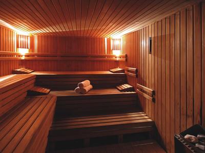 Innenraum einer Holzsauna mit mehrstufigen Sitzbänken, warmem Licht und gespaltener Holzwand.