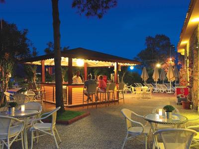 Gemütliche Außenbar mit Tischen und Stühlen, beleuchtet in der Abenddämmerung, umgeben von Bäumen.