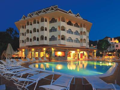 Großes Hotel mit beleuchtetem Außenpool, Liegestühlen und mehrstöckiger Fassade bei Abenddämmerung.