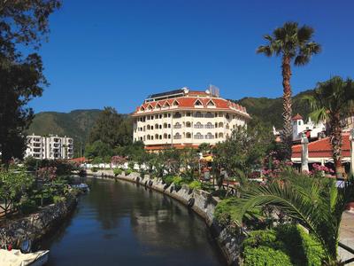 Hotel mit rotem Dach am Wasserkanal, umgeben von Palmen und grünem Garten bei blauem Himmel