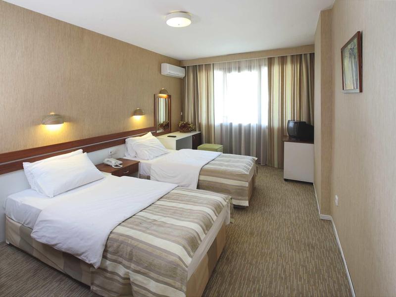 Ein schlicht eingerichtetes Hotelzimmer mit zwei Einzelbetten, Teppichboden und Fenster.